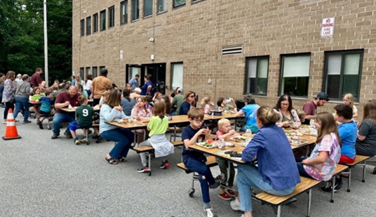 children and adults sit at cafeteria tables outside school