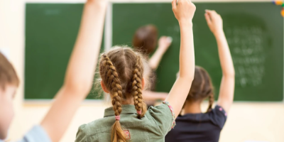 Children in a classroom raise their hands.
